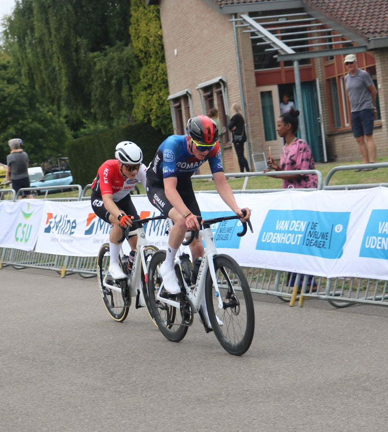 Jack Baldie cyclists racing on a road with spectators and banners in the background