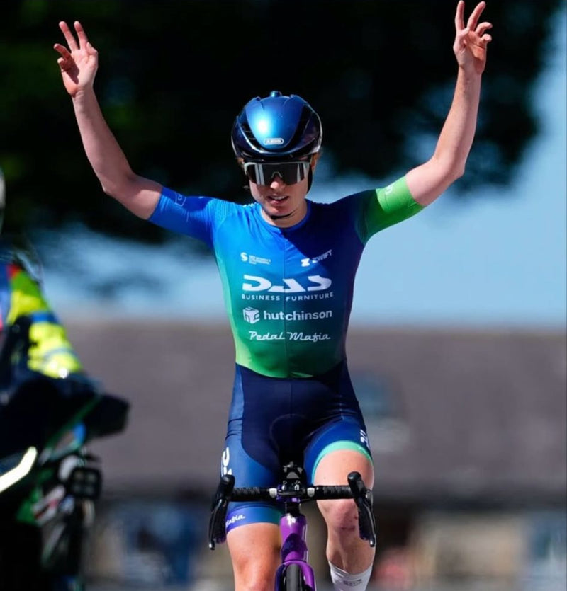 lucy lee Cyclist in a blue and green racing suit celebrating on a bike with visible branding.